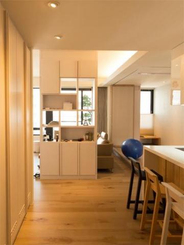 築合室內裝修設計有限公司 - 本案位於新北市重劃區社區大樓，主要成員為男女主人與2小孩，屋內採光良好，偶有親友來訪需求，室內格局方正採光充足。設計師在入口處以櫃體區隔玄關與佛堂空間，另以開放式吧檯作為緩衝，用木地板最為地界​端景設置一面具穿透性櫃體擺放紀念性物品做為裝飾，因男主人有大量物品收納需求，設計上將原本3米6長的電視主牆以拉門隱蔽的方式延伸至佛堂區至7米5長，如此大容量的收納設計使空間更為簡潔與大器。