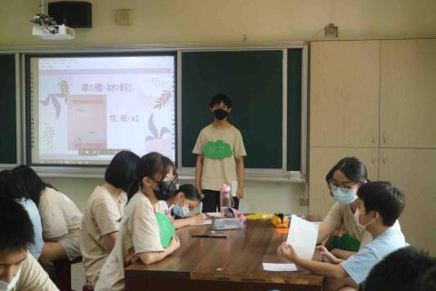 蔡佳妤 - 到偏鄉國小舉辦營隊的實際照片，圖片中是正在進行體驗活動：摺紙教學與父親節卡片製作（照片中右邊坐在藍色衣服小男孩旁邊的是我）