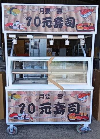 靈感製造 - 這是一台設計精美的 壽司攤車，主打 「10元壽司」。招牌採用日式風格背景，搭配生動的壽司插圖，突顯產品特色，吸引顧客目光。

設計細節描述：

主視覺元素：傳統竹編紋理背景，營造日式懷舊氛圍。
色彩搭配：使用溫暖的米色系，搭配黑色字體與壽司插圖，增強辨識度。
產品標語：醒目的「10元壽司」，讓顧客一目了然，價格透明，吸引路人。
實用性設計：攤車前方設有大型展示櫃，方便擺放壽司並保持衛生。