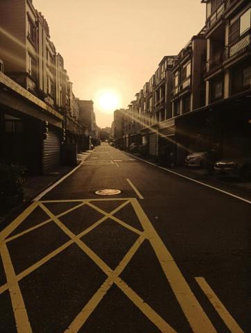 QJ攝影 - 「隨著日落，這條街道彷彿被染上了一層柔和的橙色濾鏡。溫暖的光線穿透建築物間的縫隙，在柏油路上投下美麗的光影。您可以想像，在一天的喧囂過後，這裡歸於平靜，只剩下餘暉與街景的對話。這是一幅讓人感到放鬆與沉思的畫面。」