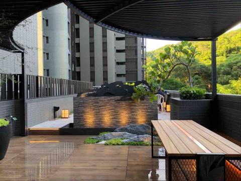 日木景觀 AZUMA - 以水瀑牆為視覺焦點，柔和燈光從牆面與步道間流動，勾勒出溫暖而靜謐的氛圍。搭配岩石造景、植栽層次與木質座椅的光影細節，整體空間展現沉穩且富質感的夜間庭園韻味，營造出放鬆、舒適的戶外休憩場景～