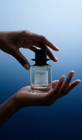 FpVisualAi - 在柔和的藍色漸層中，一雙深膚色的手優雅地捧著那瓶「FASHIONABLY KIVE」香水。上方的指尖輕輕捏住黑色高帽瓶蓋，彷彿正要揭開一場隱秘的儀式，下方的手掌則穩穩托住瓶身，將這50ml的GPU SCENT / No 01 呈獻給觀者。透明玻璃折射出清澈的光澤，液體微微透著藍綠，瓶身上的簡潔白標在靜謐的光影中格外醒目，整個畫面低調而奢華，彷彿時間在這一刻凝結，只剩下指尖與香氣之間的輕柔對話。